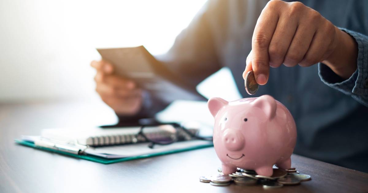 Een mannenhand die munten in een roze spaarpot stopt om geld te sparen